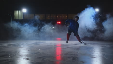 Ein-Männlicher-Eishockeyspieler-Mit-Einem-Puck-Auf-Der-Eisbahn-Zeigt,-Wie-Er-Sich-Beim-Dribbeln-Direkt-In-Die-Kamera-Bewegt-Und-Vor-Einem-Dunklen-Hintergrund-Im-Rauch-Direkt-In-Die-Kamera-Blickt